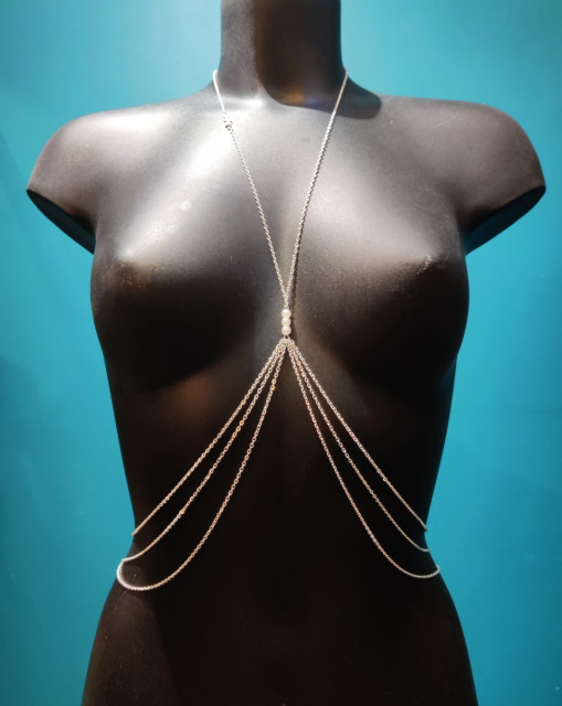 Bijou de poitrine en chaîne fine argentée avec perles blanches sur l'entre-seins et croix sur le collier.