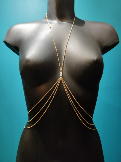 Bijou de poitrine en chaîne fine dorée avec perles blanches sur l'entre-seins et croix sur le collier.