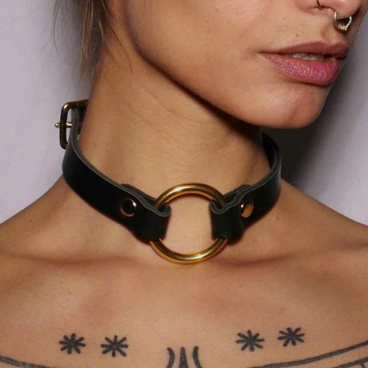 Un collier ras le cou en cuir noir avec un anneau en acier doré pour les jeux BDSM.