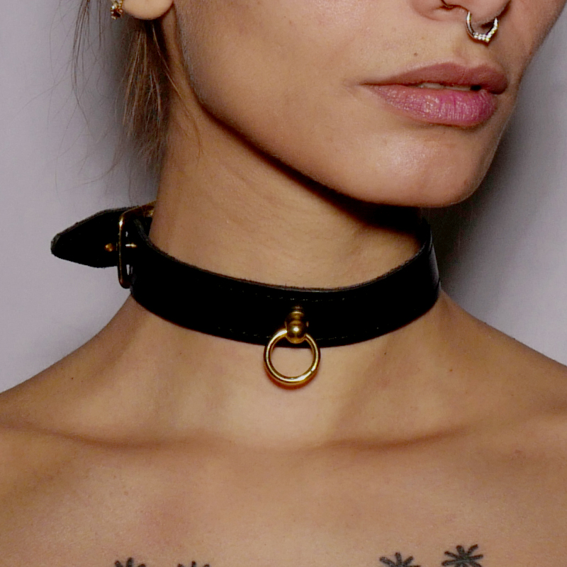 Choker fin en cuir noir surmonté d&#039;un anneau en acier doré. Il se porte comme bijou ou accessoire de jeu de soumission