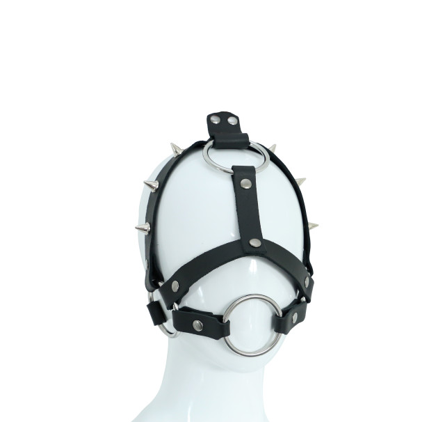 Harnais de tête en cuir noir clouté. Son anneau central peut se porter comme gag-ring.